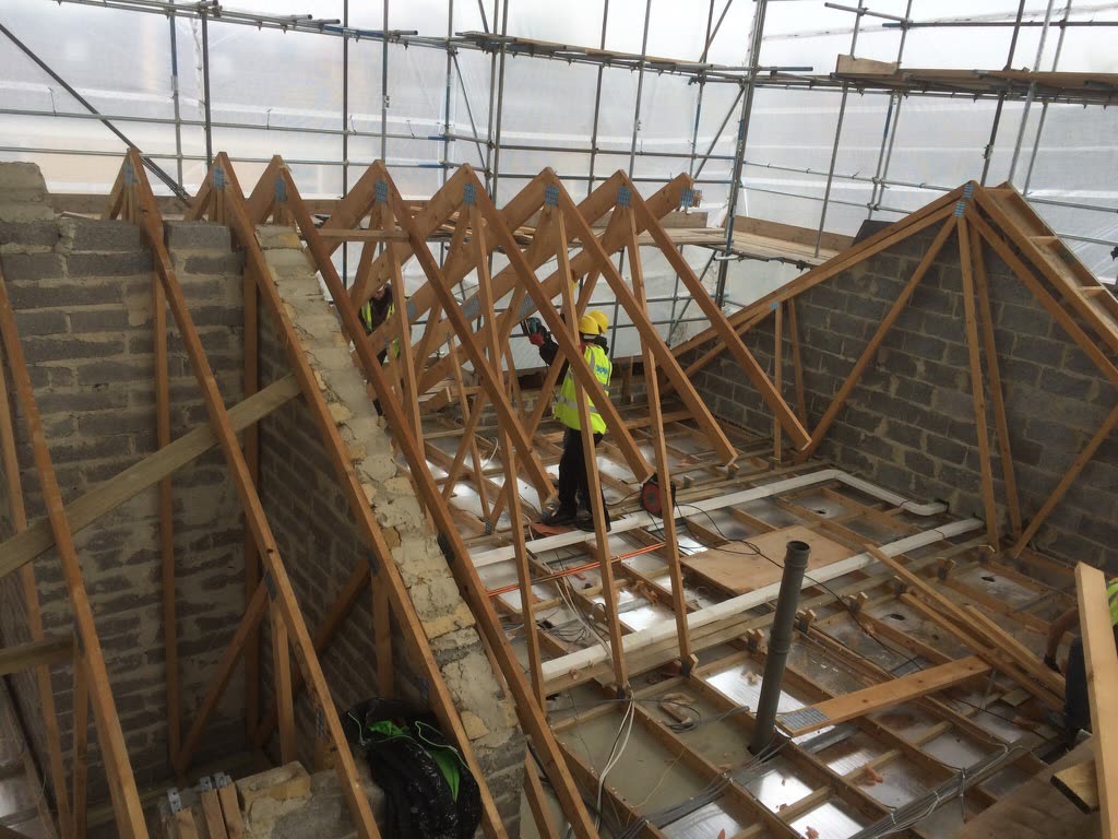 The new storey going up: timber trusses landing on the blockwork, under the temporary roof that kept the weather off the flats below.